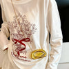 A person wearing a white long-sleeve shirt with a graphic design and a gold metal clutch bag.