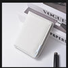 A white slim vertical men's card wallet resting on a white surface next to a black pen and a Vogue magazine.