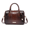 A dark brown crocodile pattern luxury handbag with a leather handle and gold hardware.