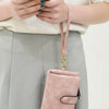 A light pink multi-slot card wallet is shown hanging from a strap against a gray skirt.