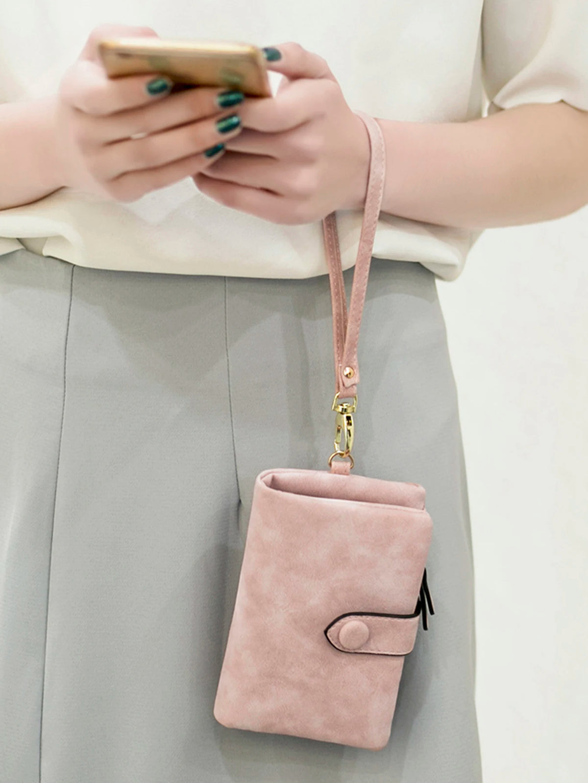 A light pink multi-slot card wallet is shown hanging from a strap against a gray skirt.