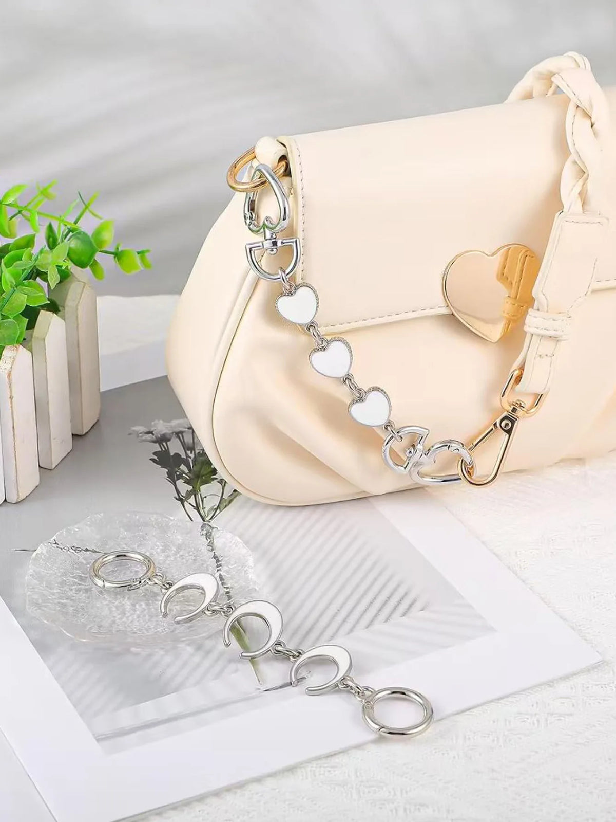 Un sac à main en cuir beige avec un extender de chaîne doré, à côté d'un bijou à chaîne argentée.