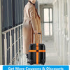 A woman in a beige coat is pulling a black suitcase with bright orange identification straps down a hallway.