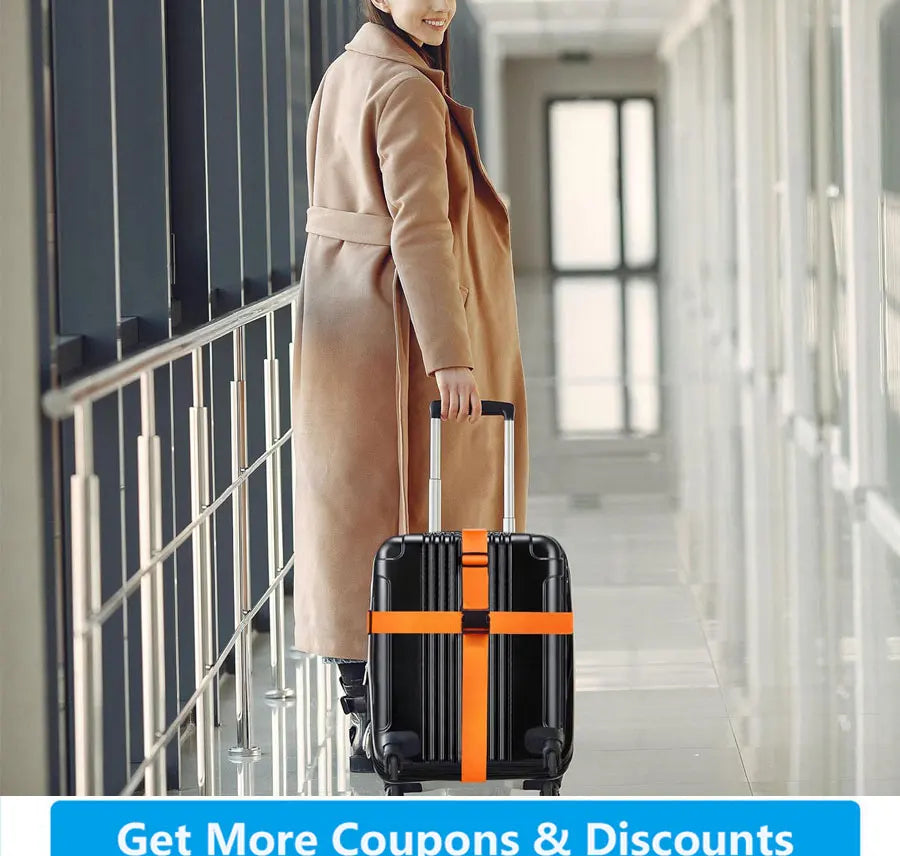 A woman in a beige coat is pulling a black suitcase with bright orange identification straps down a hallway.