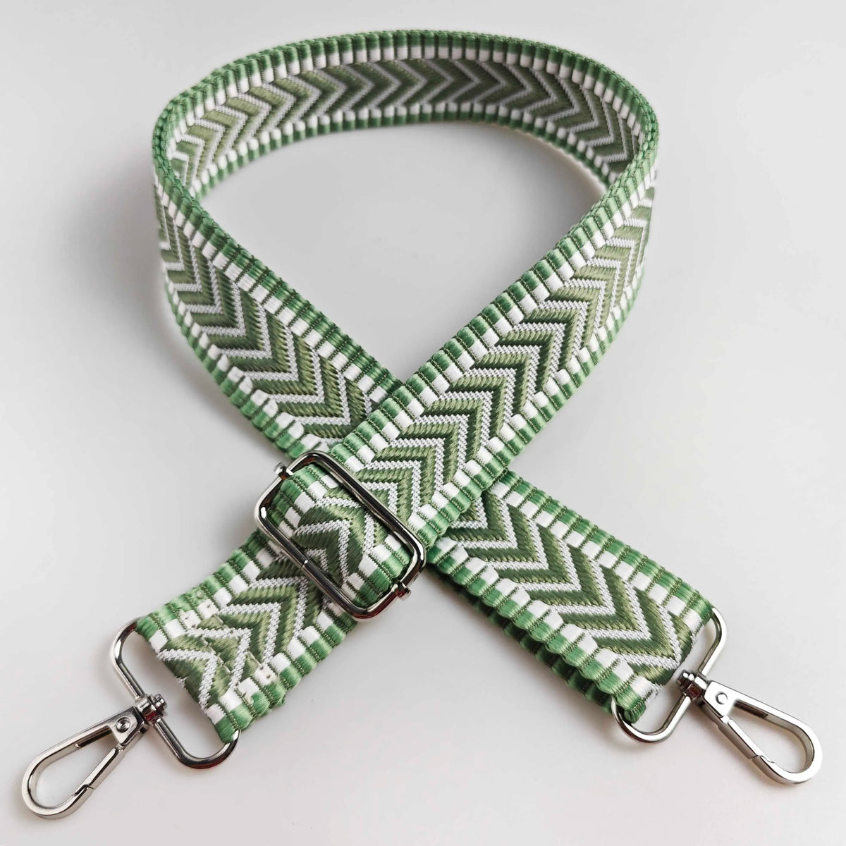A close-up of a wide adjustable handbag strap featuring an arrow jacquard pattern in green and white.