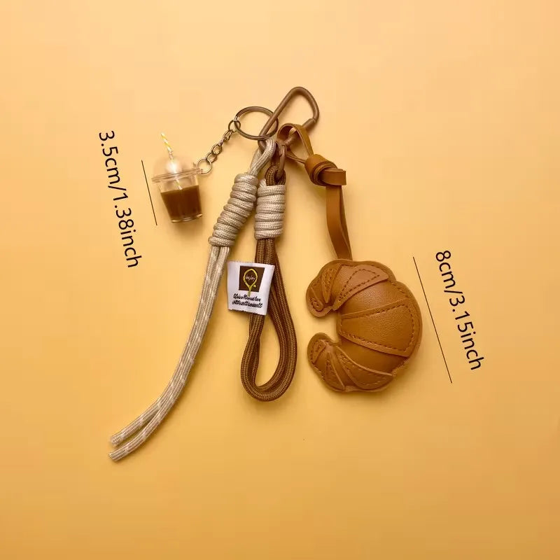 A brown leather croissant shaped keychain with a lanyard and pendant on a beige background.