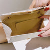 A hand holds a light beige glitter pleated crossbody clutch bag with a gold chain detail.