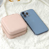 A light pink compact leather jewelry travel box next to a blue smartphone on a white textured fabric.