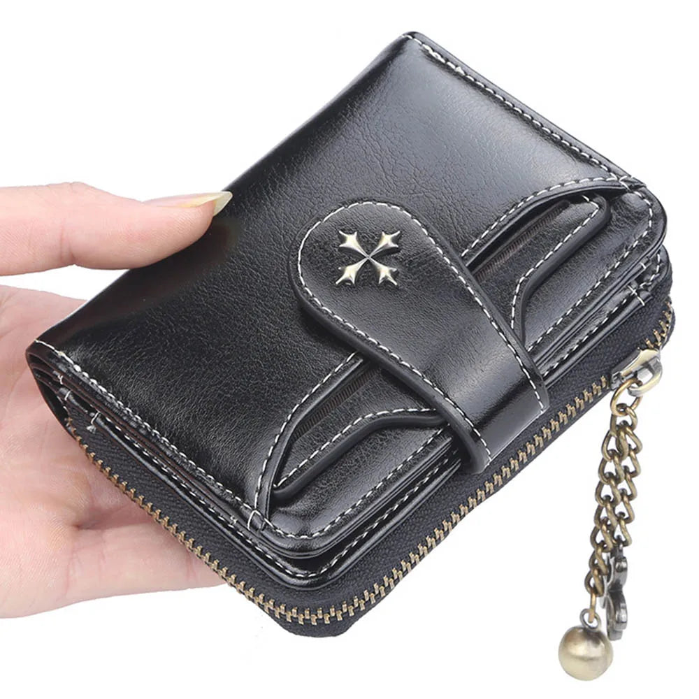 A black PU leather compact wallet with a flap closure and a gold-toned chain is being held by a hand.