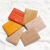 A collection of five genuine leather zipper card holders in shades of orange, beige, and pink stacked on a white background.