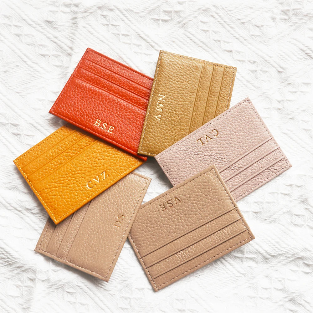 A collection of five genuine leather zipper card holders in shades of orange, beige, and pink stacked on a white background.