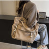 A person is holding a beige corduroy shoulder bag with a zipper on a dark surface.