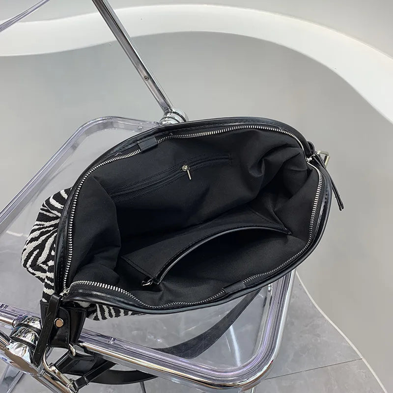 Schwarze Leinencoffertasche mit Zebraprint, über der Schulter, auf einem klaren Ständer präsentiert.