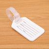 A white plastic luggage tag with a clear strap and lines for writing name, address, and state, resting on a wooden surface.