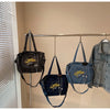 A display of women's denim crossbody bags hanging on a metal rack against a light wall.