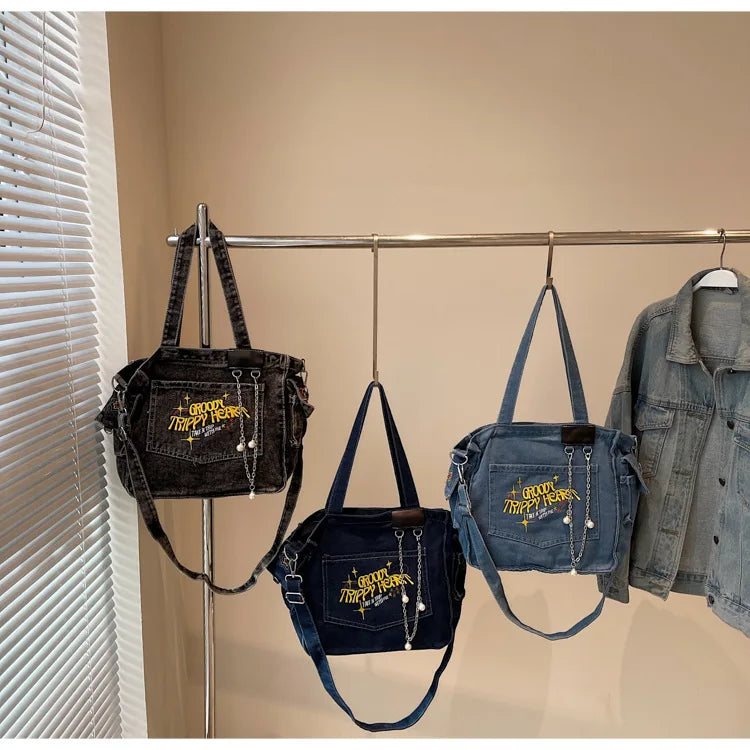 A display of women's denim crossbody bags hanging on a metal rack against a light wall.