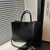 A black tote bag with a leather strap is displayed next to a framed document.