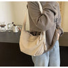 A person wearing a gray sweatshirt holds a beige canvas crossbody shoulder bag.
