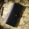 A black genuine leather long bi-fold wallet with a snap closure resting on aged parchment paper.