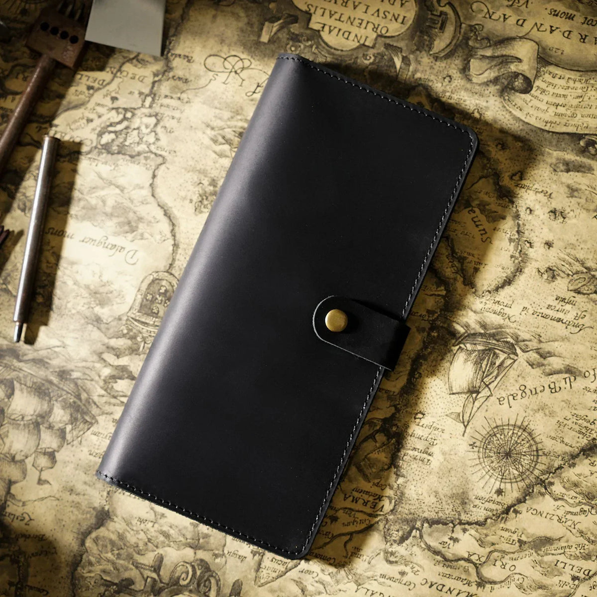 A black genuine leather long bi-fold wallet with a snap closure resting on aged parchment paper.