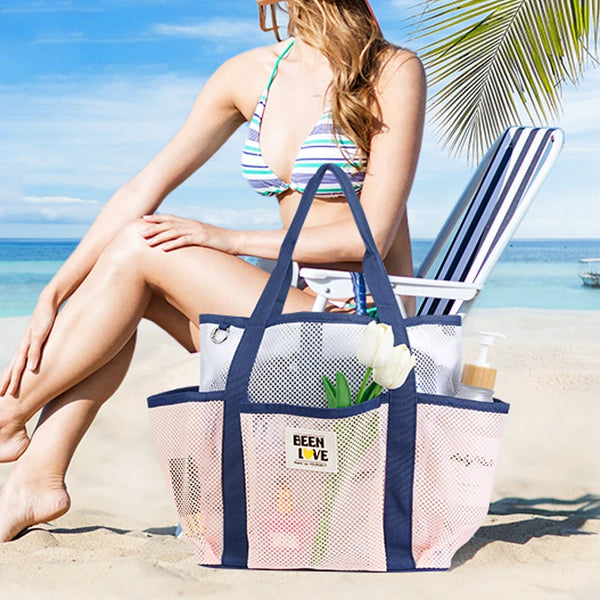 A woman relaxing on the beach holding a navy mesh tote bag with a white floral design.
