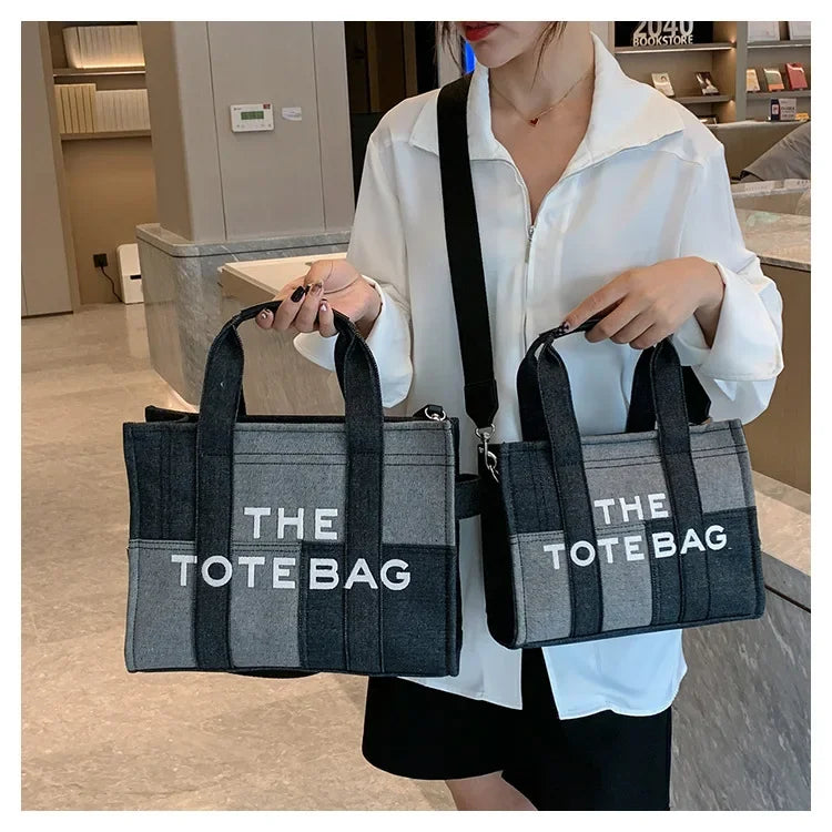 A woman holds a black and gray tote bag with white text in a casual setting.