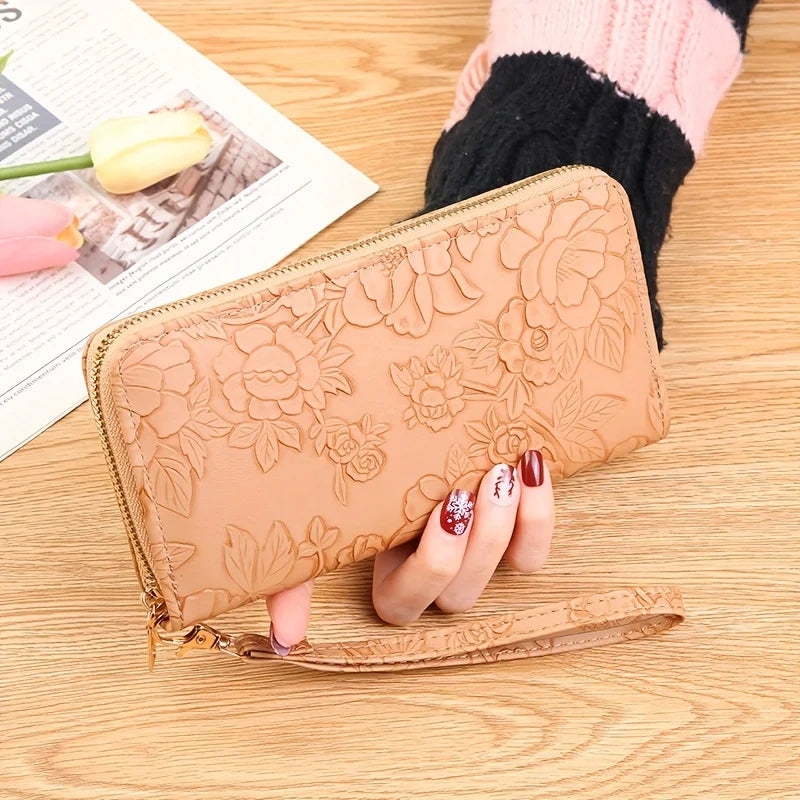 Cartera de tarjeta de cuero PU floral repujado color marrón, apoyada sobre una superficie de madera junto a una manga de punt
