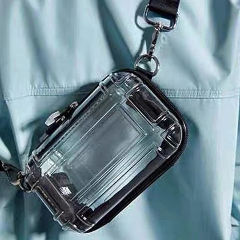 A clear transparent shoulder crossbody cosmetic bag with a black strap is shown against a light blue fabric background.