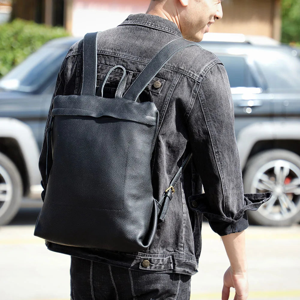 A man wearing a black leather backpack and denim jacket stands next to a dark SUV.
