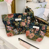 A floral patterned velvet cosmetic pouch in teal and pink resting on a white surface.