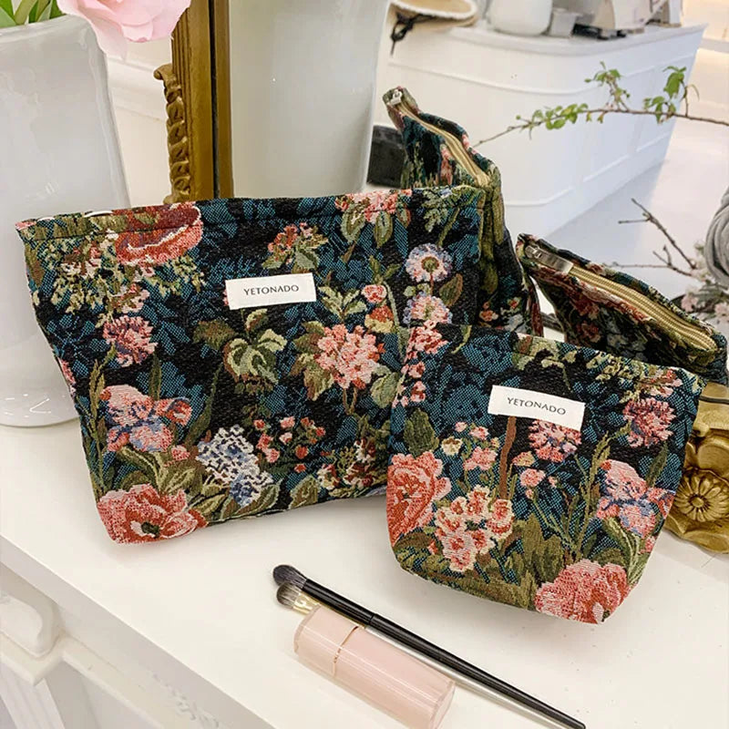 A floral patterned velvet cosmetic pouch in teal and pink resting on a white surface.