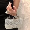 A hand holds an elegant diamond rhinestone evening clutch bag with a golden tassel against a light marble background.