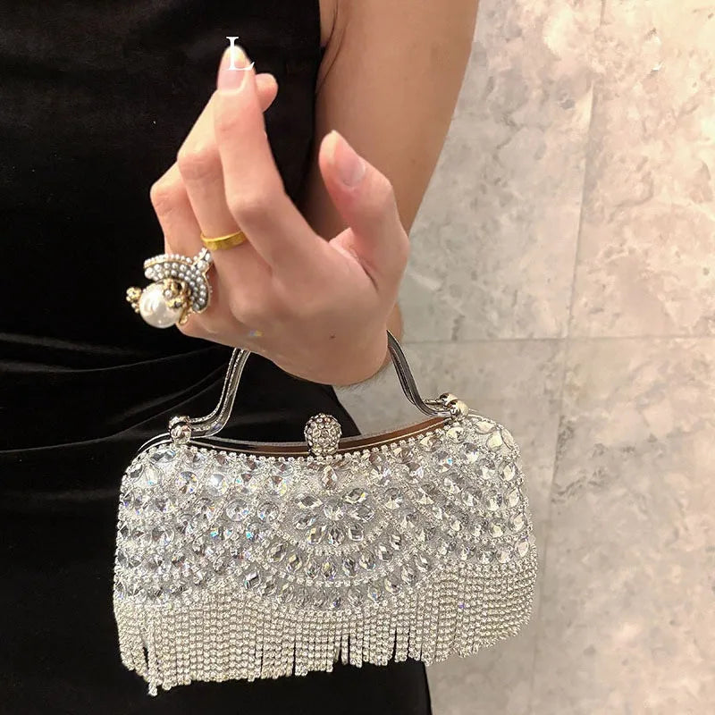 A hand holds an elegant diamond rhinestone evening clutch bag with a golden tassel against a light marble background.