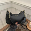 A black leather shoulder bag with a gold chain detail is held by a hand against a light background.