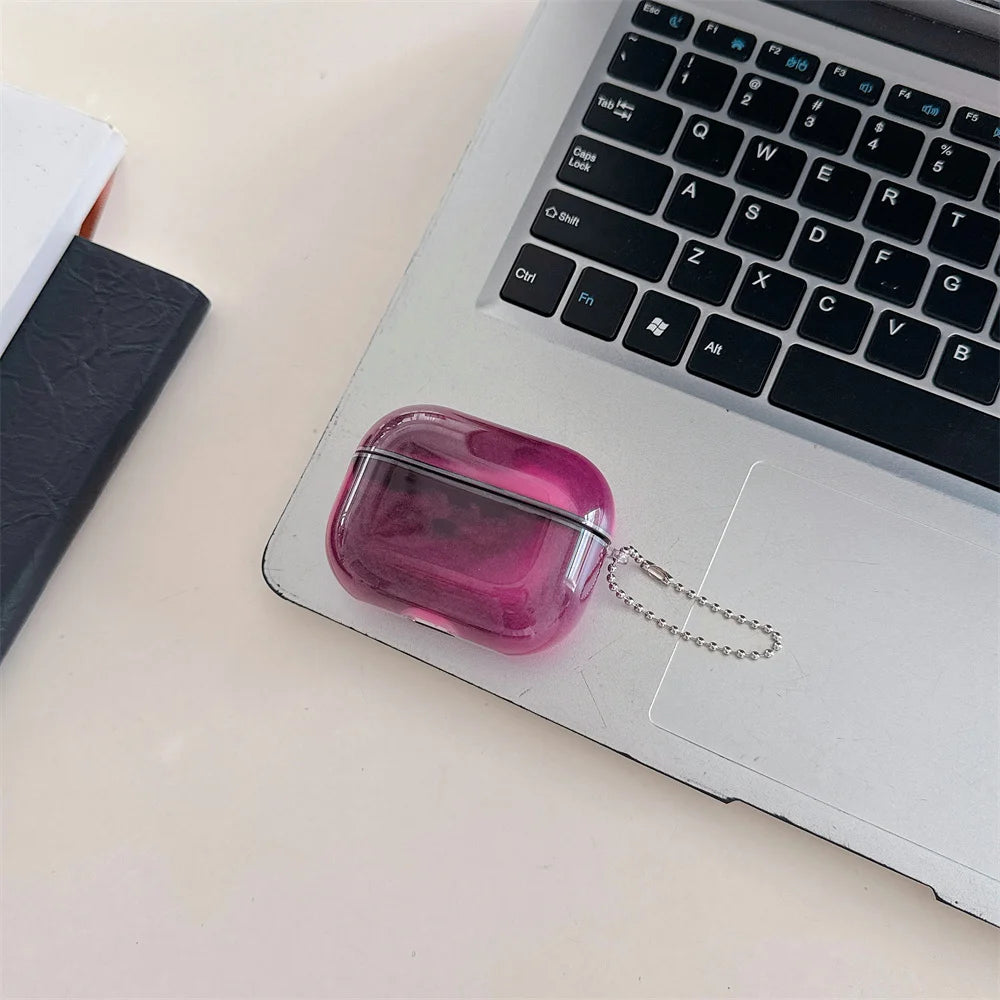 A small, translucent pink luminous sand effect case for AirPods rests on a silver laptop keyboard.