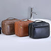 Three cosmetic organizer bags in brown and black leather are displayed next to a white sink and faucet.