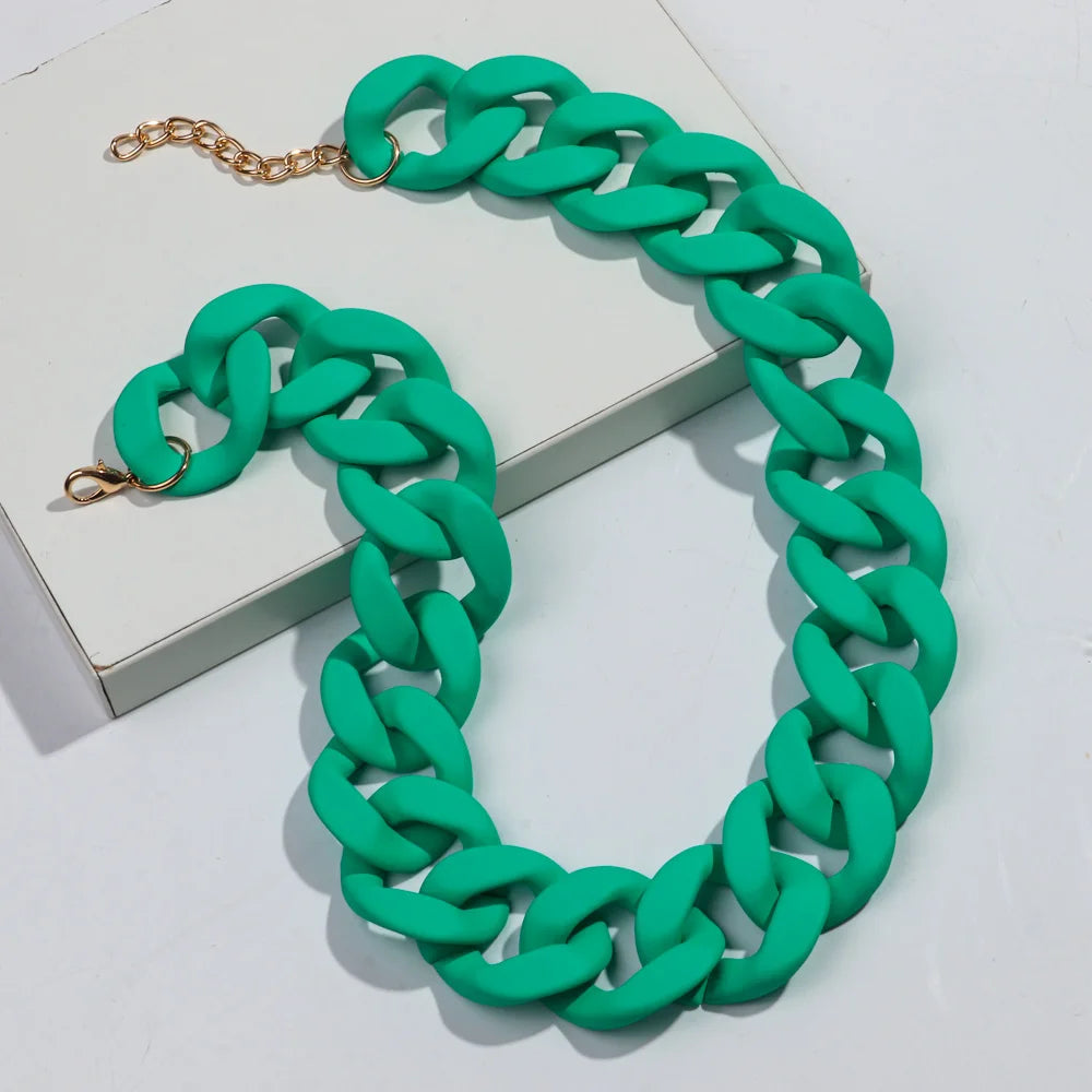 A green matte acrylic chain necklace with a gold-tone clasp is displayed on a white box.
