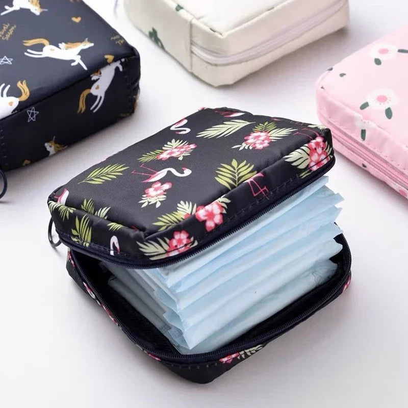 A black compact pouch filled with light blue sanitary pads is shown next to a pink storage pouch.