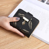 Cartera clutch de cuero PU negro con detalles en hoja de oro, sostenida por una mano sobre una superficie de madera.