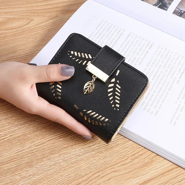 Cartera clutch de cuero PU negro con detalles en hoja de oro, sostenida por una mano sobre una superficie de madera.