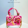 A pink floral clutch bag with gold sequins and embroidery is displayed against a light background.
