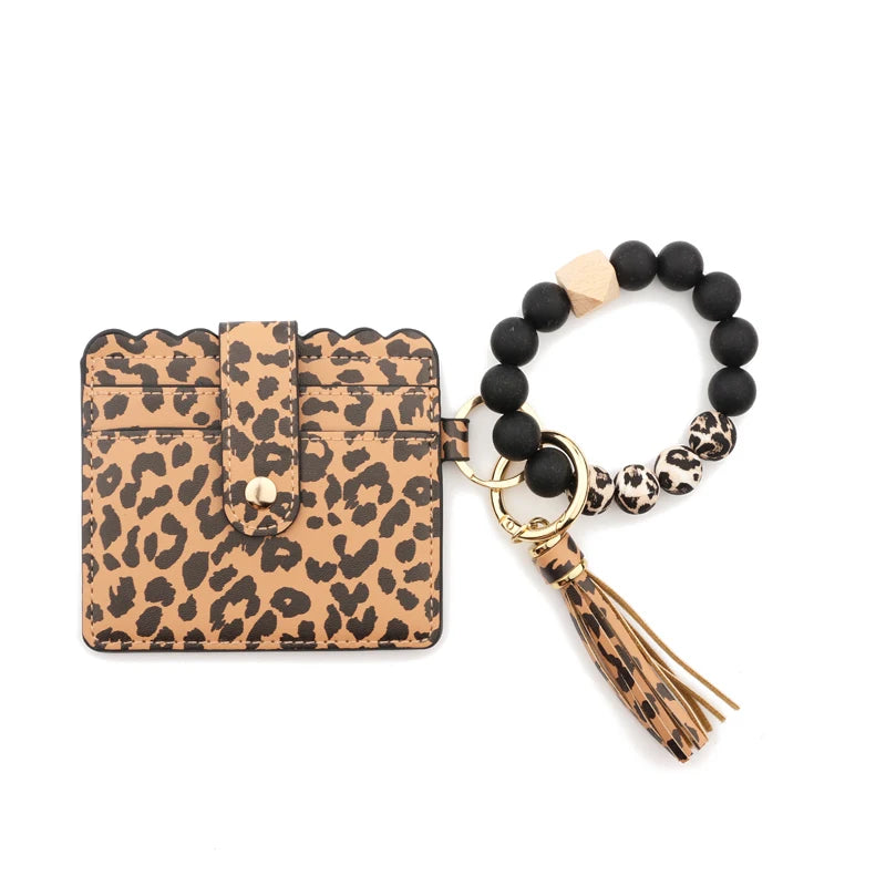 A black silicone bead bracelet is displayed next to a tan leather card holder with a leopard print design.