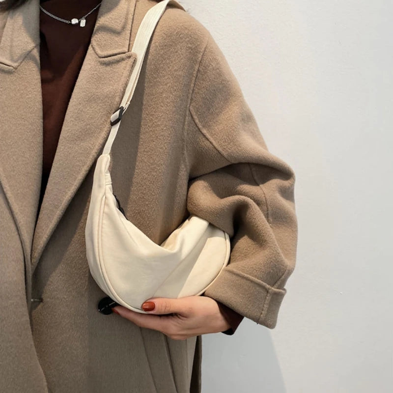 A beige wool coat with a cream sling crossbody bag is shown on a person's shoulder.