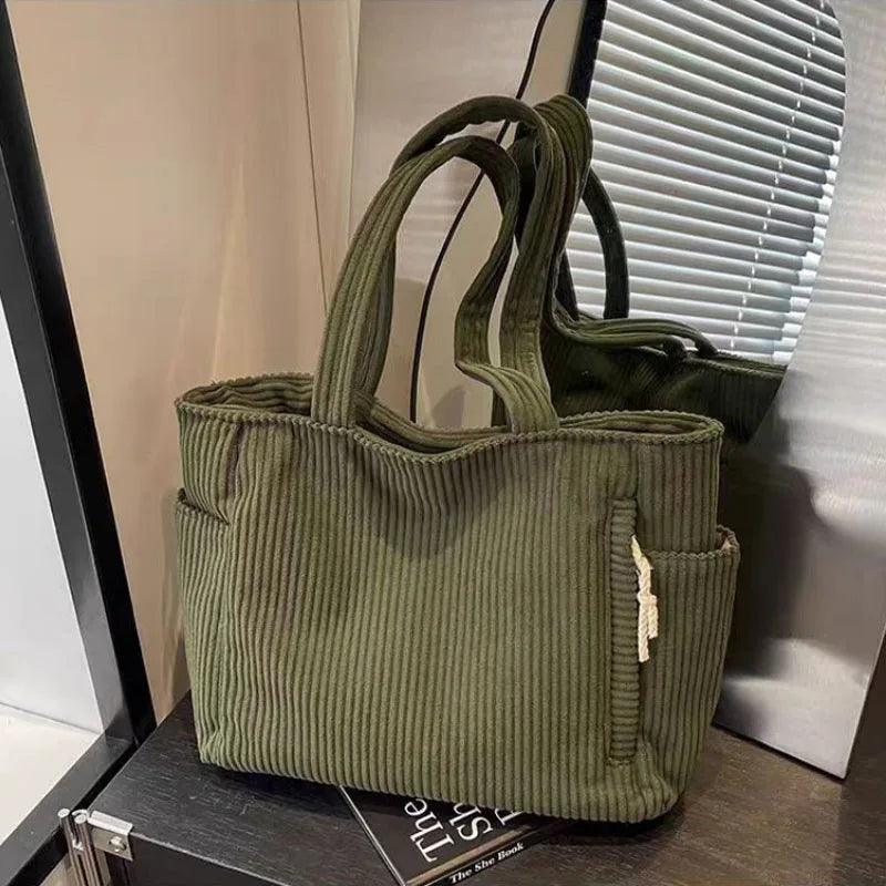 A olive green corduroy shoulder bag with a zipper is displayed against a light background.