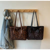 Two leopard print vintage tote bags are hanging on a wooden rack against a white wall.