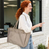 Two women are standing in a modern office setting, one pointing toward a beige laptop tote bag.
