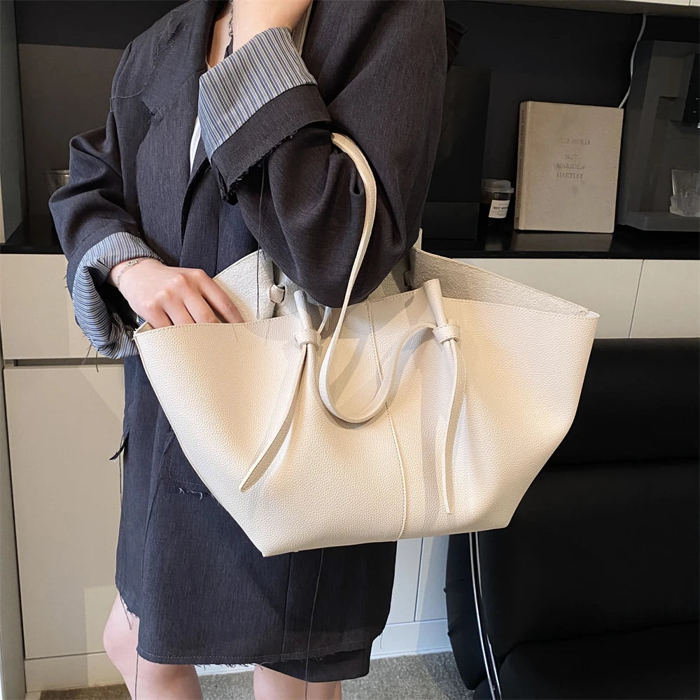 A woman holds a white luxury PU leather shoulder tote bag in front of her while standing indoors.