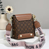 Sac bandoulière en similicuir marron avec quincaillerie dorée et sangle rose posé sur une surface blanche.
