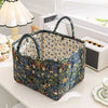 A quilted fabric storage basket with carry handles featuring a blue and green floral pattern sits on a white surface.