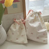 Two light pink canvas makeup bags tied with pink ribbon resting on a white surface next to a yellow flower.